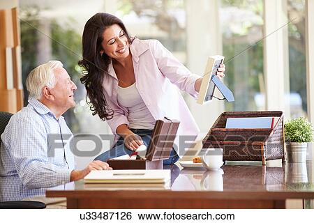 Stock Photograph - Senior Father Looking At Photo In Frame With Adult Daughter. Fotosearch
