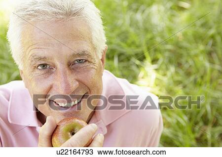 Stock Image - Senior man eating apple outdoors. Fotosearch