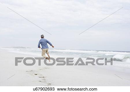 Stock Image - Senior man running and jumping on beach. Fotosearch