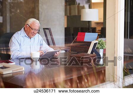 Stock Image - Senior Man Using Digital Tablet Through Window. Fotosearch