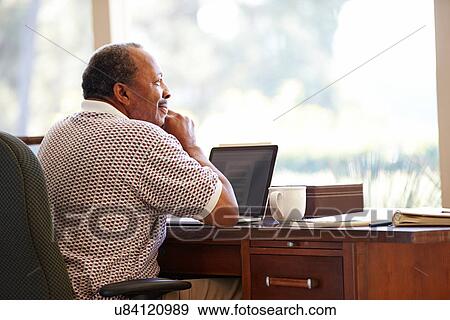 Stock Photo - Senior Man Using Laptop On Desk At Home. Fotosearch