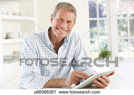 Stock Image - Senior man using tablet at home. Fotosearch