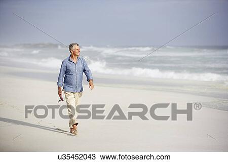 Stock Image - Senior man walking on beach. Fotosearch
