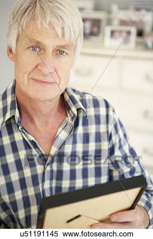 Stock Photography - Senior man with photographs at home. Fotosearch