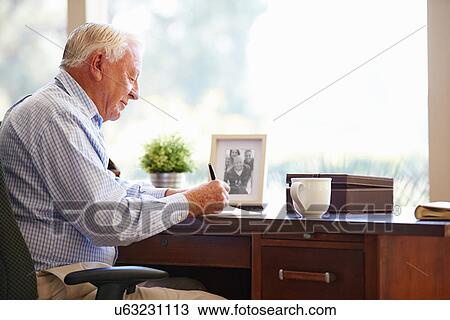 Stock Image - Senior Man Writing Memoirs In Book Sitting At Desk. Fotosearch