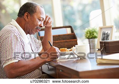 Stock Image - Senior Man Writing Memoirs In Book Sitting At Desk. Fotosearch
