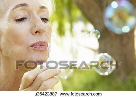 Stock Photo - Senior woman blowing bubbles outdoors. Fotosearch