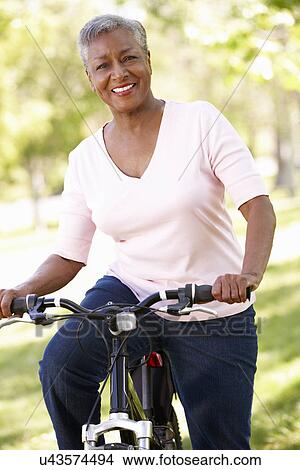 Picture - Senior woman cycling in park. Fotosearch