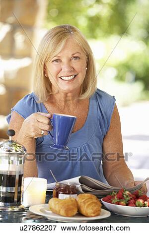Stock Photo - Senior woman eating breakfast outdoors. Fotosearch
