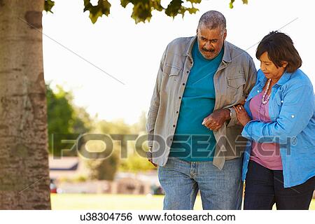 Stock Photograph - Senior Woman Helping Husband As They Walk In Park Together. Fotosearch