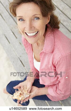 Stock Photo - Senior woman holding seashell. Fotosearch