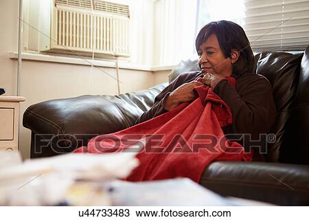 Stock Image - Senior Woman Trying To Keep Warm Under Blanket At Home. Fotosearch