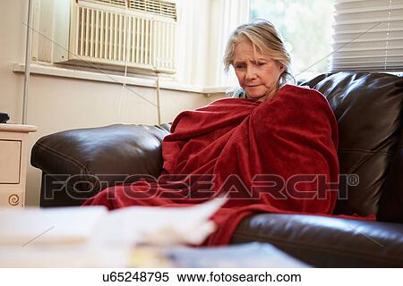 Stock Photography - Senior Woman Trying To Keep Warm Under Blanket At Home. Fotosearch