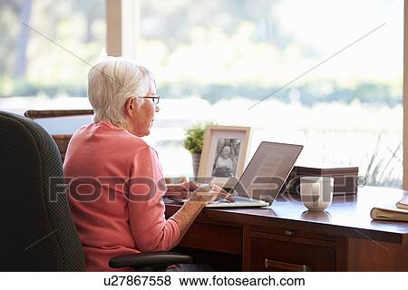 Stock Photo - Senior Woman Using Laptop On Desk At Home. Fotosearch