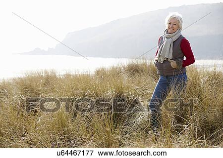Stock Photo - Senior Woman Walking Through Sand Dunes On Winter Beach. Fotosearch