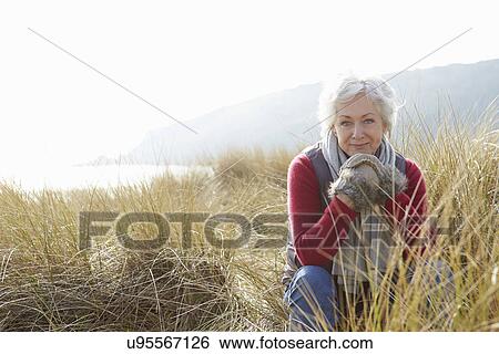 Stock Photograph - Senior Woman Walking Through Sand Dunes On Winter Beach. Fotosearch