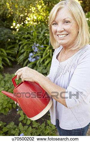 Stock Image - Senior woman watering garden. Fotosearch