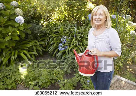 Stock Image - Senior woman watering garden. Fotosearch
