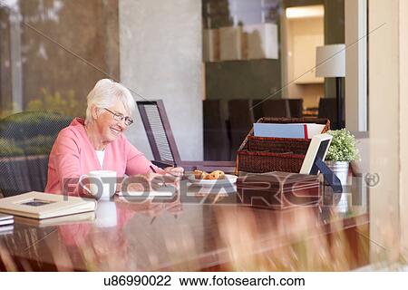 Stock Image - Senior Woman Writing Memoirs In Book At Desk. Fotosearch