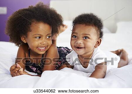 Stock Image - Sister With Baby Brother Lying On Parent's Bed. Fotosearch