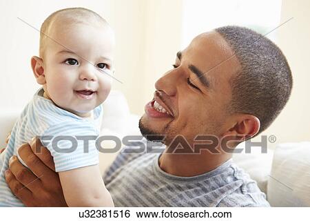 Stock Photograph - Smiling Father Playing With Baby Son At Home. Fotosearch