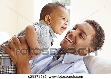 Stock Photography - Smiling Father Playing With Baby Son At Home. Fotosearch