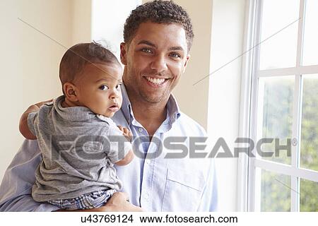 Picture - Smiling Father Standing By Window With Baby Son At Home. Fotosearch