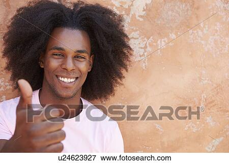 Stock Photo - Smiling Man Leaning Against Wall Giving Thumbs Up . Fotosearch
