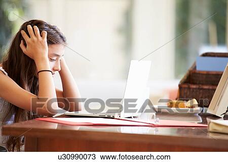 Stock Image - Stressed Teenage Girl Using Laptop On Desk At Home. Fotosearch
