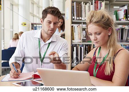 Stock Image - Teacher Helping College Student With Studies In Library. Fotosearch
