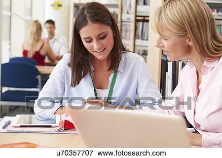 Stock Photo - Teacher Helping College Student With Studies In Library. Fotosearch