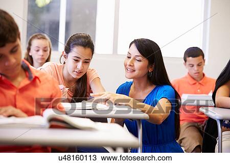 Stock Image - Teacher Helping Female High School Student In Classroom. Fotosearch