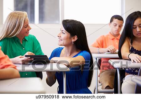 Stock Photo - Teacher Helping Female High School Student In Classroom. Fotosearch