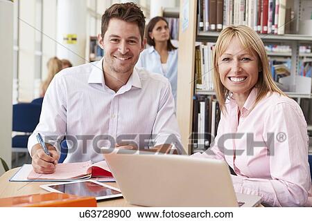 Stock Image - Teacher Helping Mature Student With Studies In Library. Fotosearch