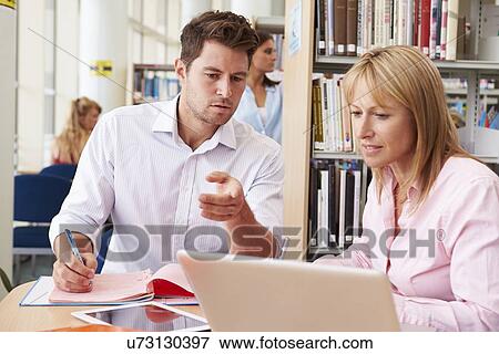 Stock Photo - Teacher Helping Mature Student With Studies In Library. Fotosearch