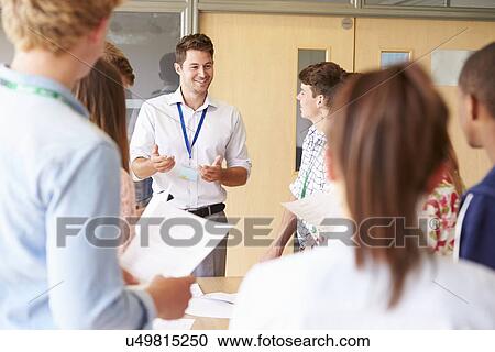 Stock Image - Teacher With College Students Standing By Desks In Classroom. Fotosearch