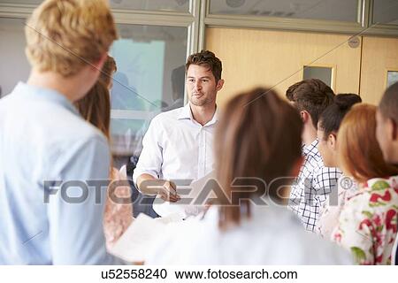 Stock Image - Teacher With College Students Standing By Desks In Classroom. Fotosearch