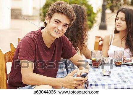 Teenage Boy Using Mobile Phone Sitting At Cafe With Friends View Large Photo Image Stock Photograph - Teenage Boy Using Mobile Phone Sitting At Cafe With Friends. Fotosearch