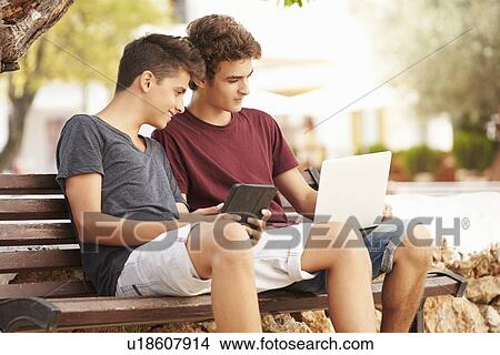 Teenage Boys On Park Bench Using Laptop And Digital Tablet View Large Photo Image Picture - Teenage Boys On Park Bench Using Laptop And Digital Tablet. Fotosearch