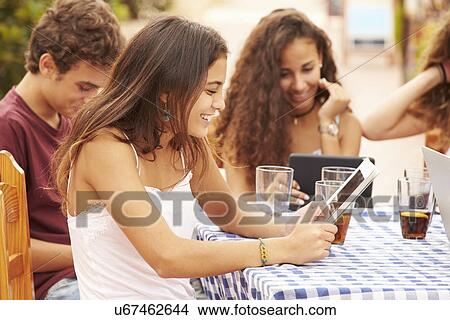 Teenage Friends Sitting At Cafe Using Digital Devices View Large Photo Image Picture - Teenage Friends Sitting At Cafe Using Digital Devices. Fotosearch