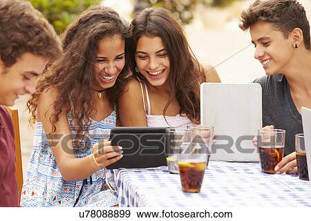 Teenage Friends Sitting At Cafe Using Digital Tablets View Large Photo Image Stock Photo - Teenage Friends Sitting At Cafe Using Digital Tablets. Fotosearch