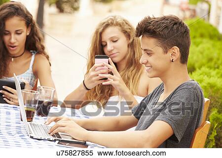 Stock Photography - Teenage Friends Sitting At Cafe Using Digital Devices. Fotosearch
