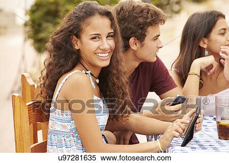 Teenage Friends Sitting At Cafe Using Digital Devices View Large Photo Image Stock Photography - Teenage Friends Sitting At Cafe Using Digital Devices. Fotosearch