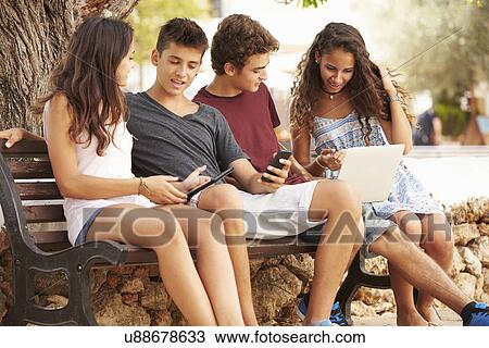 Teenage Friends Sitting In Park Using Digital Devices View Large Photo Image Stock Image - Teenage Friends Sitting In Park Using Digital Devices. Fotosearch