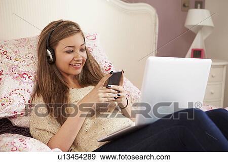 Stock Photo - Teenage Girl Lying On Bed Using Laptop Whilst Texting. Fotosearch