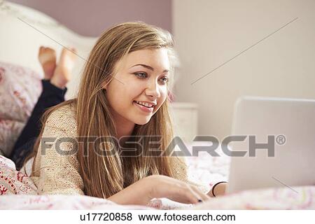 Stock Photo - Teenage Girl Lying On Bed Using Laptop. Fotosearch