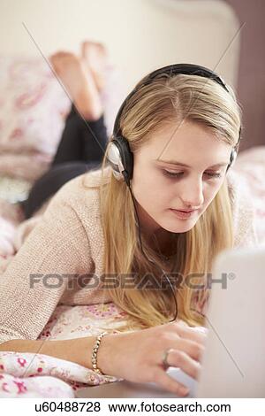 Teenage Girl Lying On Bed Using Laptop Wearing Headphones View Large Photo Image Stock Photo - Teenage Girl Lying On Bed Using Laptop Wearing Headphones. Fotosearch