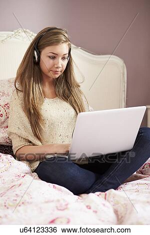 Teenage Girl Lying On Bed Using Laptop Wearing Headphones View Large Photo Image Stock Photograph - Teenage Girl Lying On Bed Using Laptop Wearing Headphones. Fotosearch