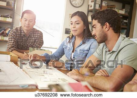 Stock Photo - Three Architects Sitting Around Table Having Meeting. Fotosearch