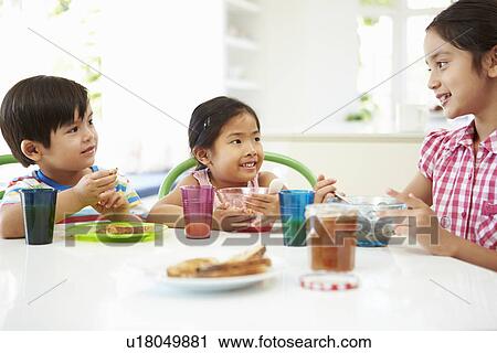 Stock Image - Three Asian Children Having Breakfast Together In Kitchen. Fotosearch